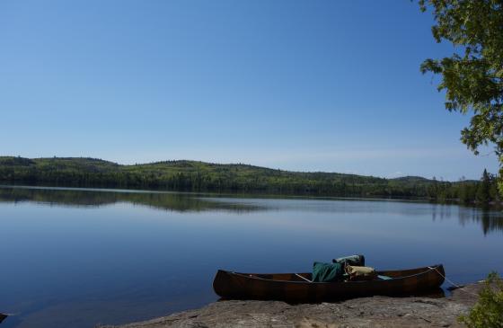 Photo of canoe on shore infront of bright blue sky reflecting on water