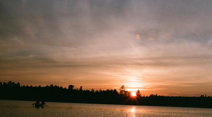 Film picture of soft orange Boundary Waters sunset with silhouette of person paddling canoe