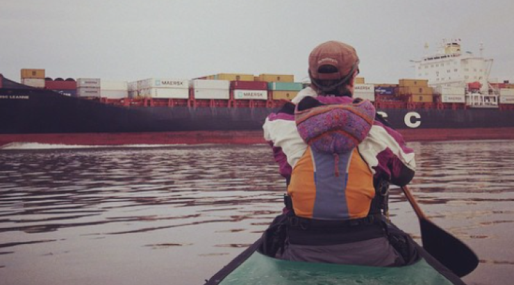 Photo of Amy Freeman paddling in a kayak towards a shipping barge