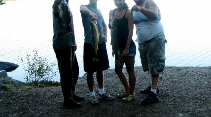 Photo of 4 people holding out fish near waters edge