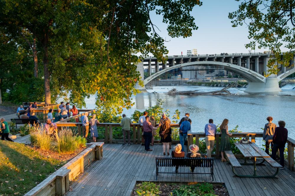 People standing on deck by river during sunset 