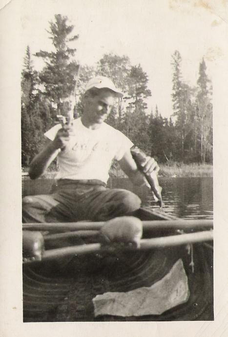 A man sits in the stern of a canoe as he pulls a fish out of the water.