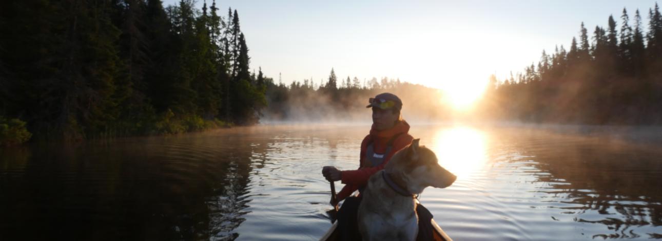 Woman and a dog in a canoe paddling during sunset.